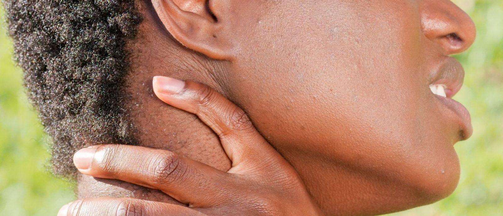 Person wincing and gripping the side of their neck below the ear