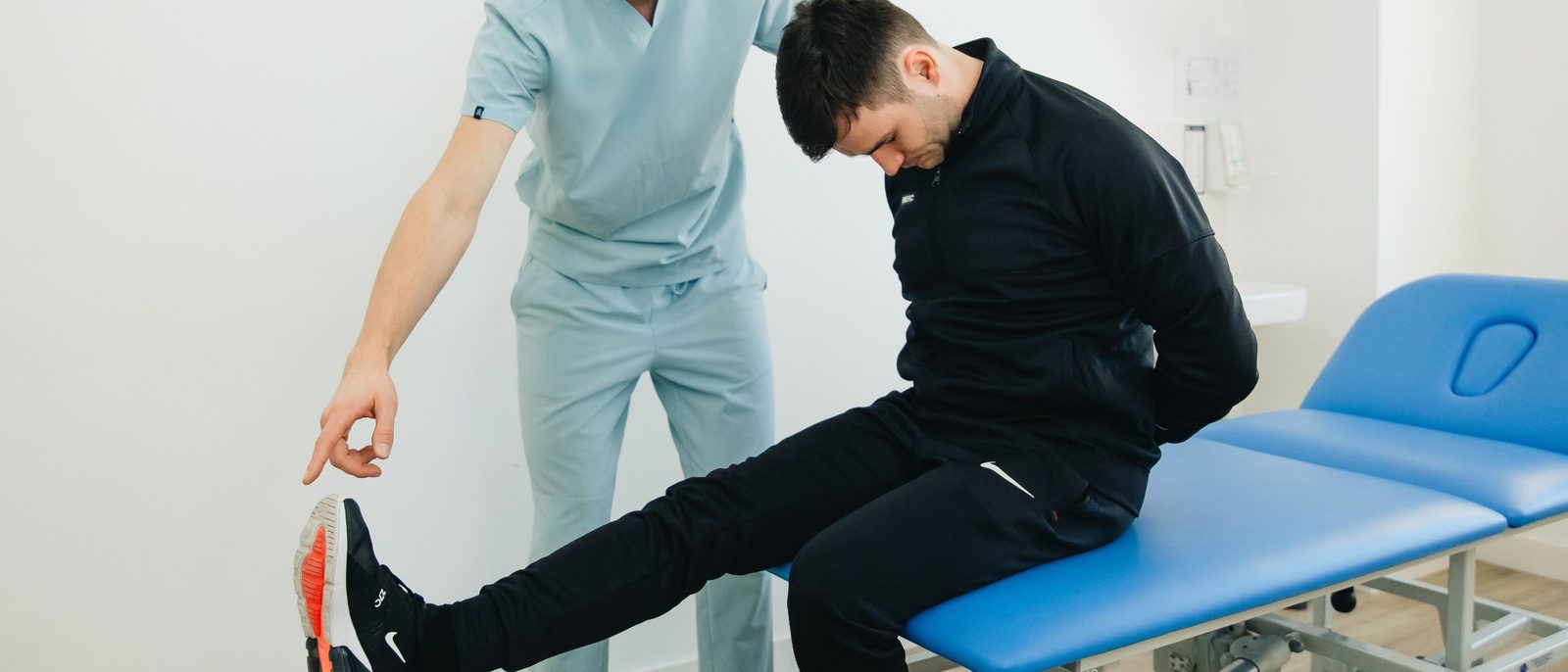 A physiotherapist guiding a seated client through a nerve tension test, leg straight and head bowed